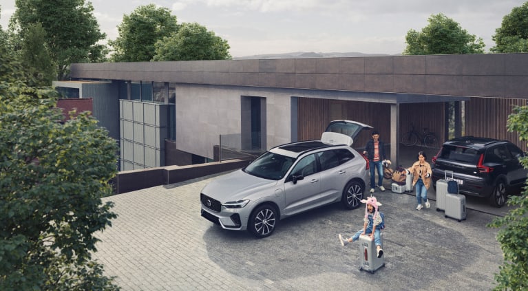 A family unloading items out of the back of a grey Volvo SUV parked near a house