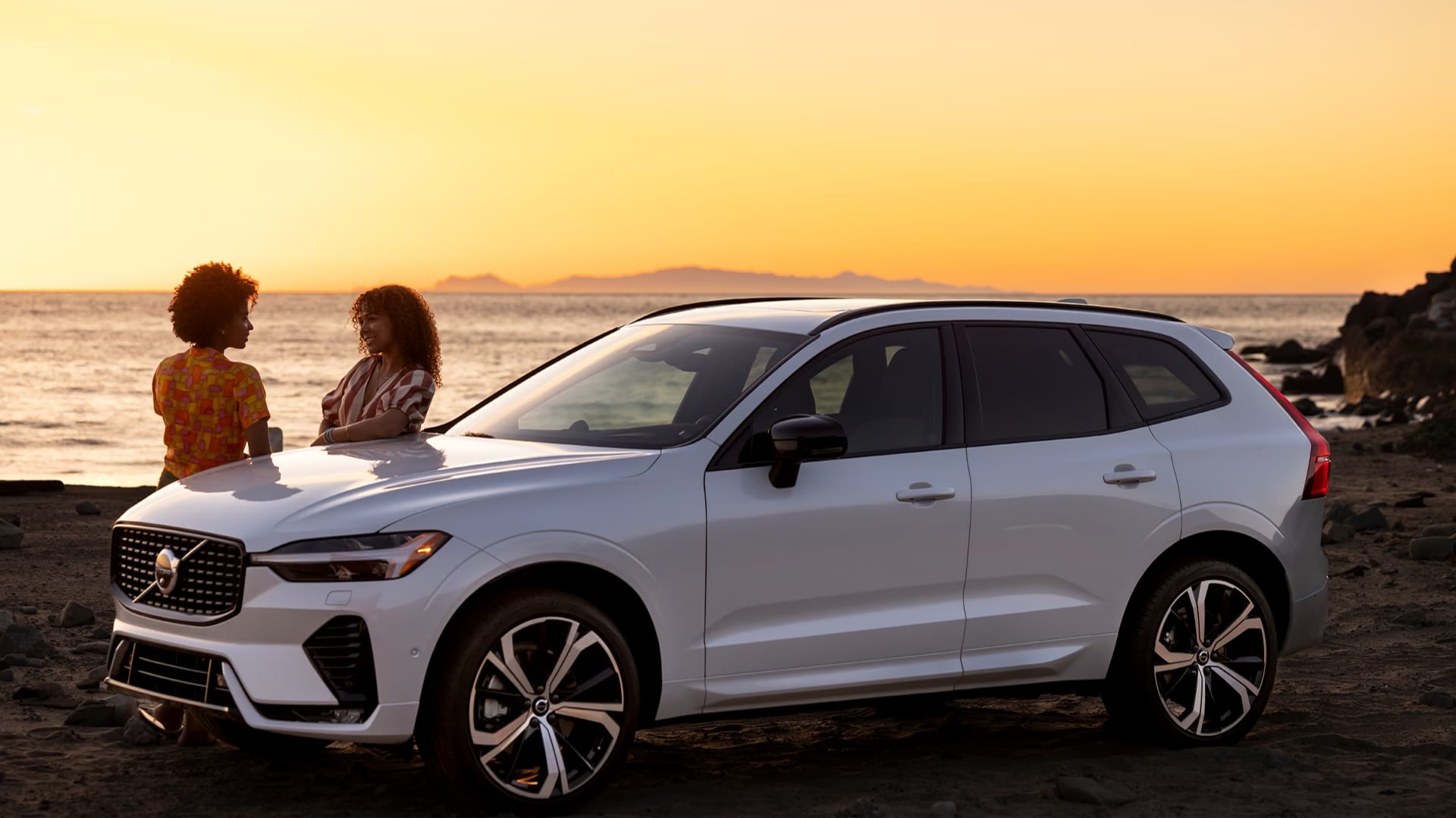 Two women talking next to a Volvo SUV on the beach