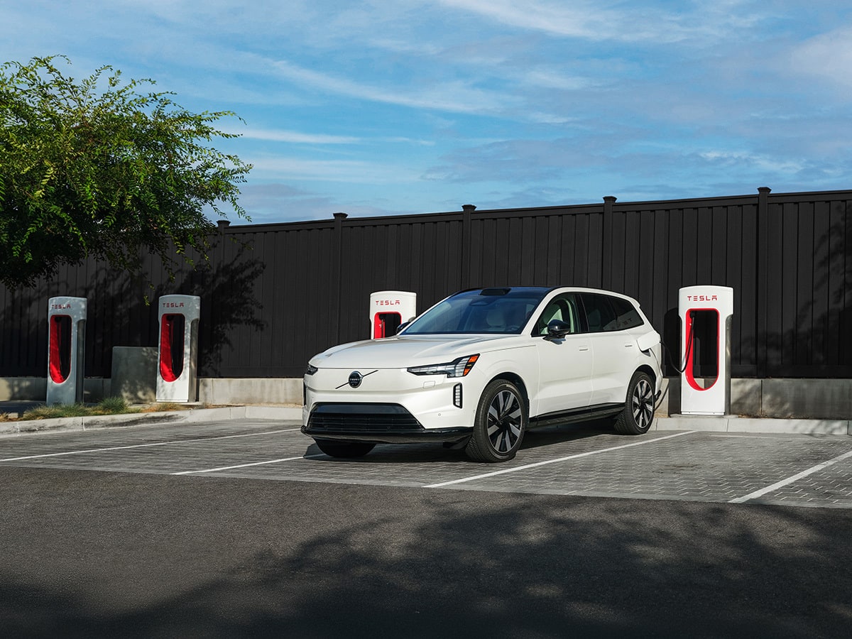 White Volvo EX90 charging in a lot of Tesla Superchargers